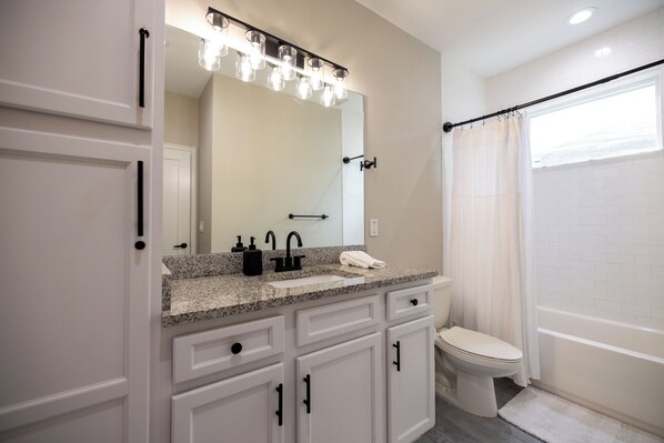 A modern bathroom with a granite countertop, a large mirror, a toilet, and a bathtub.