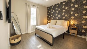 Ein Schlafzimmer mit Bett, Nachttisch, Wand-TV, Deckenventilator und einem Fenster mit Vorhängen.