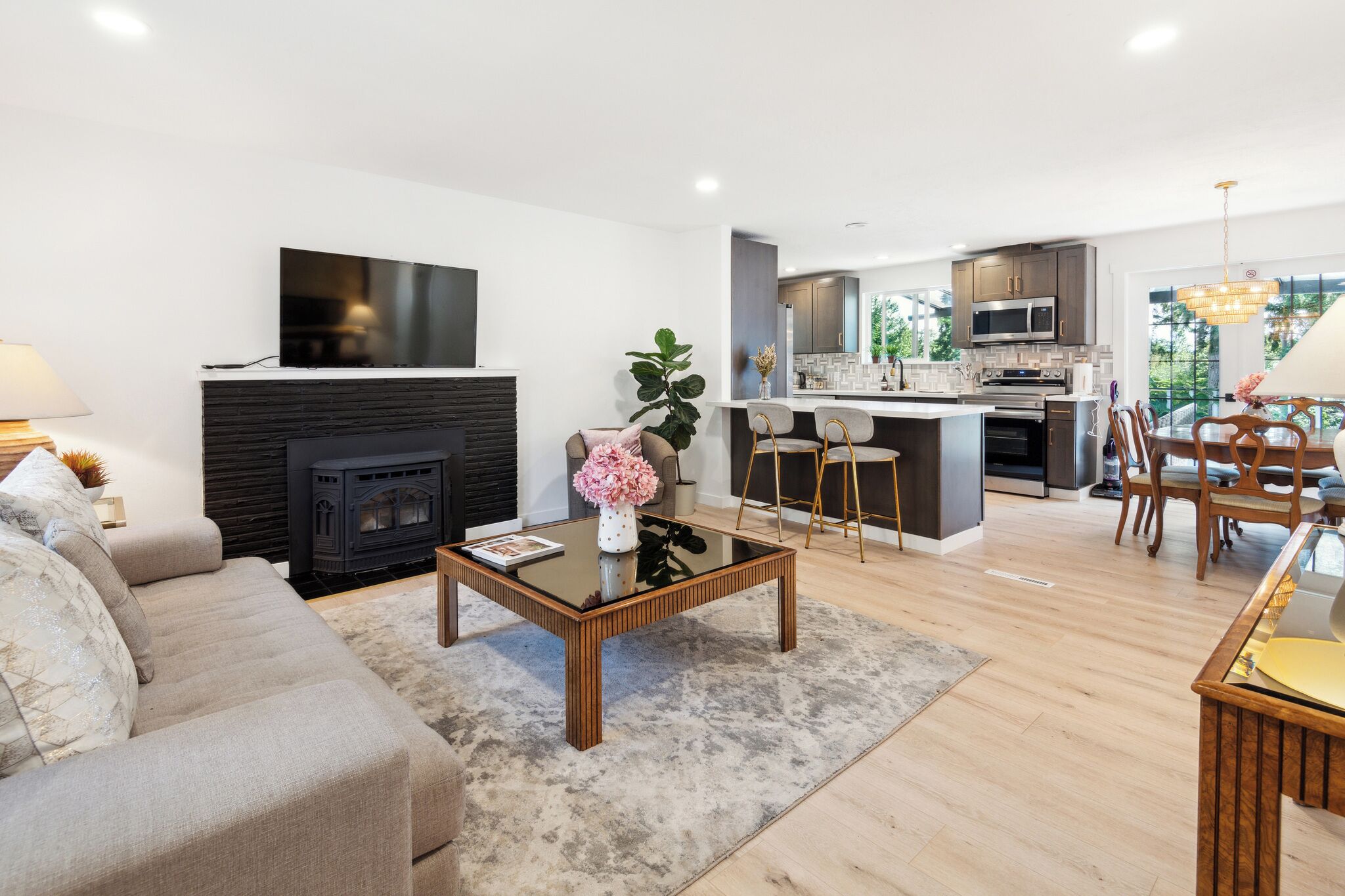 A modern living room with a fireplace, a dining area with a chandelier, and a kitchen with a large island.