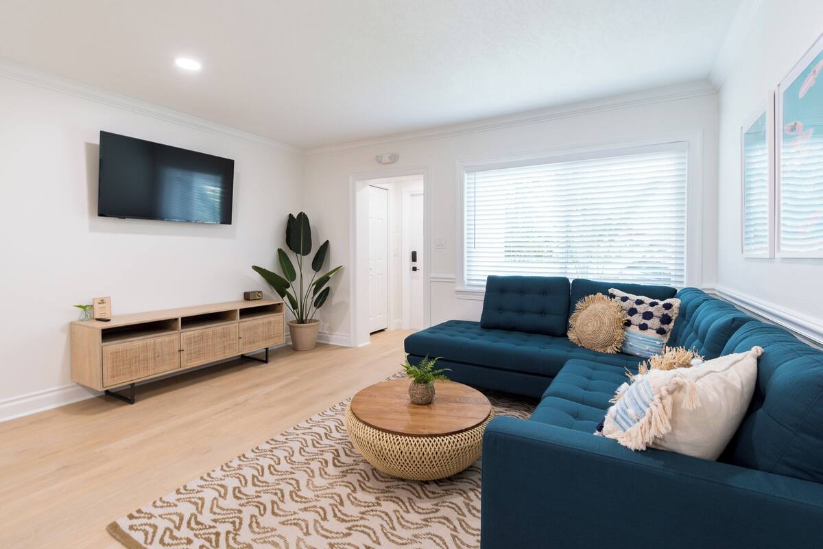 A modern living room with a blue sofa, a wooden coffee table, and a TV mounted on the wall.