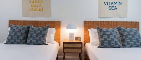 Une chambre avec un lit double doté d’une tête de lit en bois, une table de chevet avec une lampe, et deux panneaux décoratifs au mur portant les inscriptions « de belles journées ensoleillées à venir » et « VITAMINE MER ».