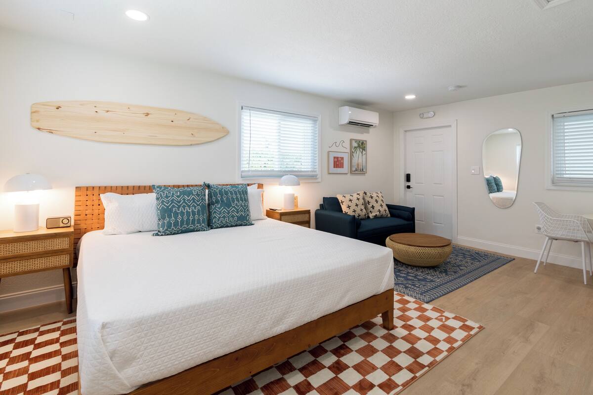 A bedroom with a wooden bed, a blue sofa, a round wicker ottoman, and a checkered rug.
