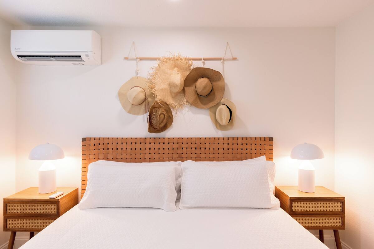 A neatly made bed with white linens, two bedside tables with lamps, and a wall-mounted air conditioner.