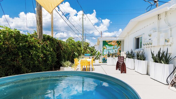 A swimming pool with a patio area, a building with a mural, and potted plants. - The Juni (Cocoa Beach)