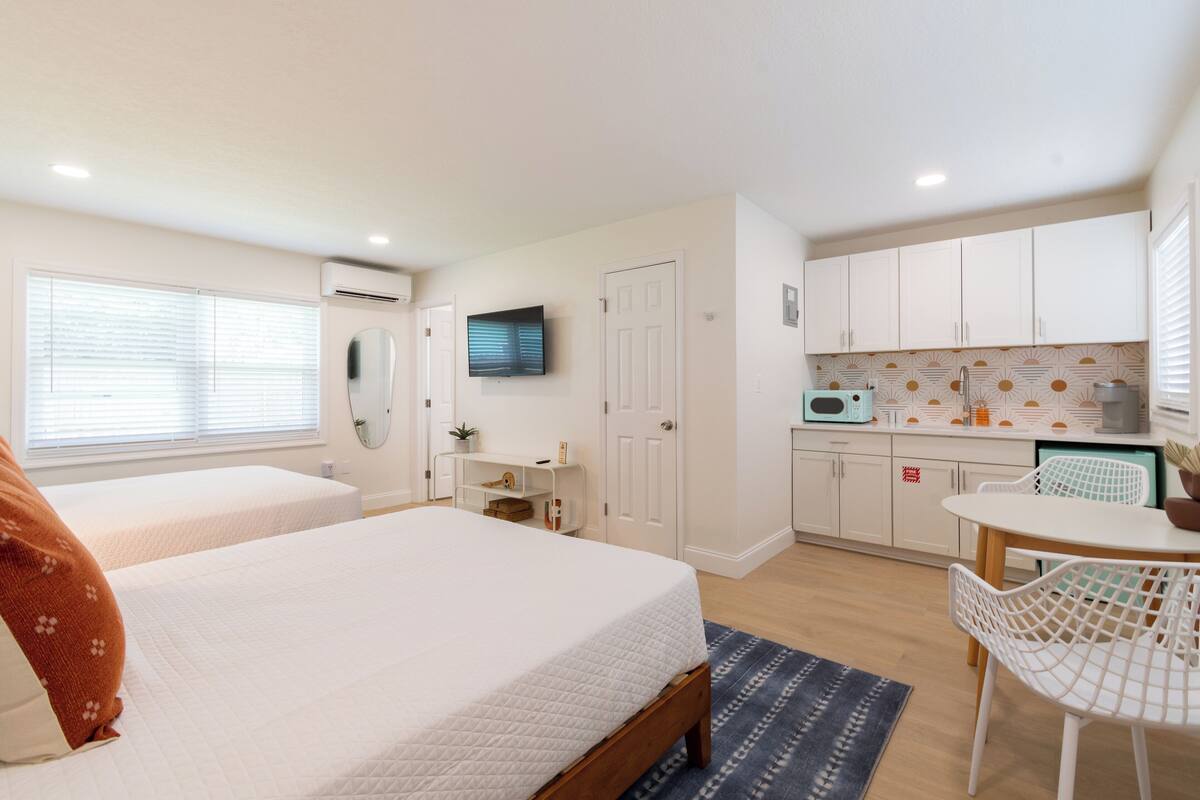 A bedroom with two beds, a small kitchenette, and a dining area with a table and chairs.