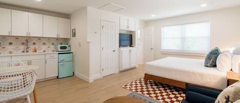 A compact, well-lit room with a kitchenette, a bed with a blue mattress, and a small dining area.