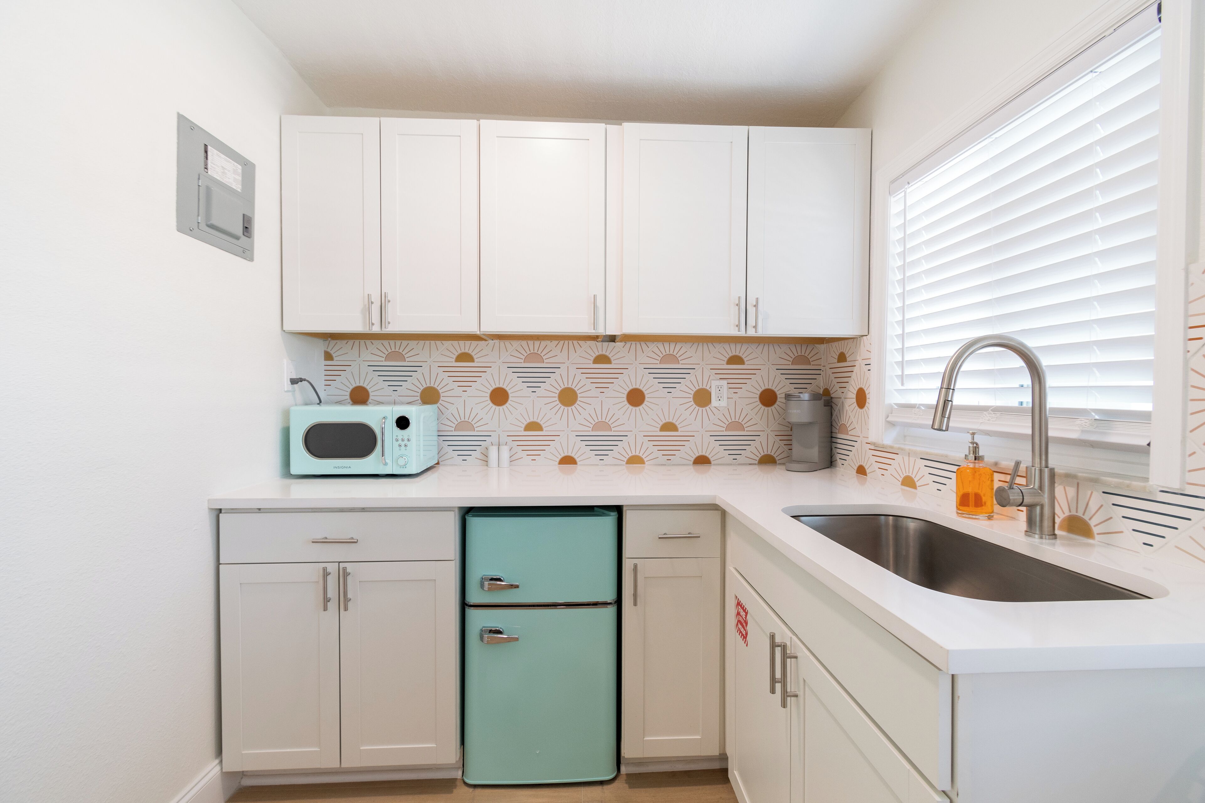 A compact kitchen with white cabinets, a teal refrigerator, and a sink with a faucet.