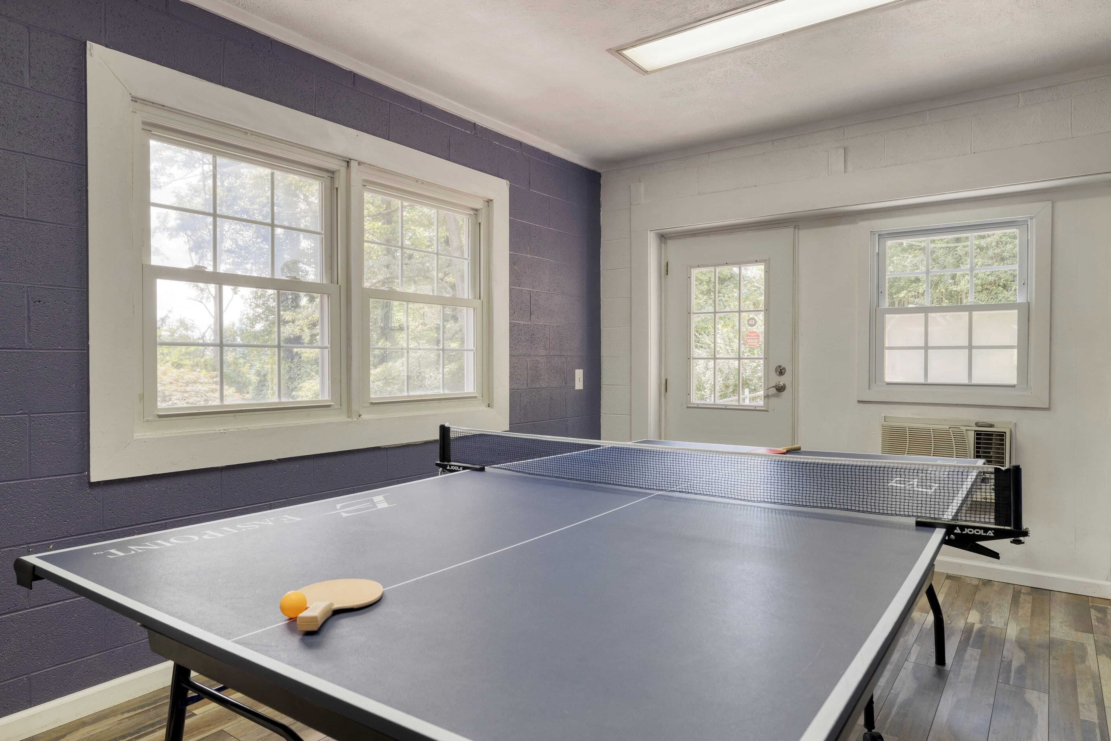 A ping pong table in a room with two windows and a door.