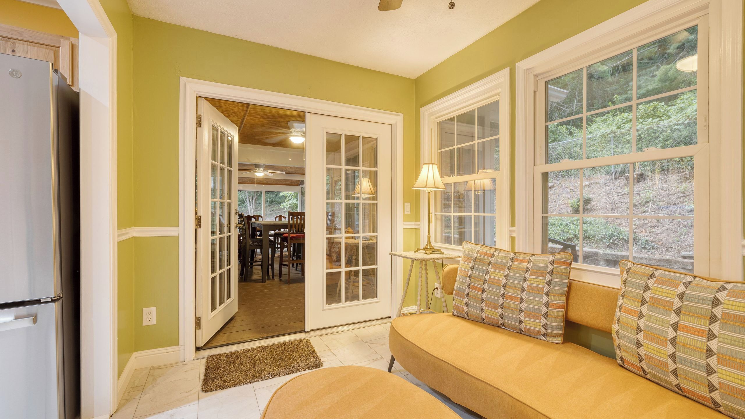 A kitchen with a refrigerator, a dining area with chairs and a table, and a sofa with patterned cushions.