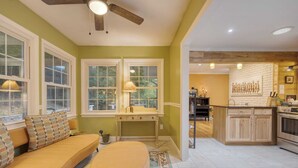 A kitchen with a wooden island, a dining area with a sofa and ottoman, and a window with a view of greenery. - Asheville Sunset 10min to Asheville + Ping Pong (Asheville)