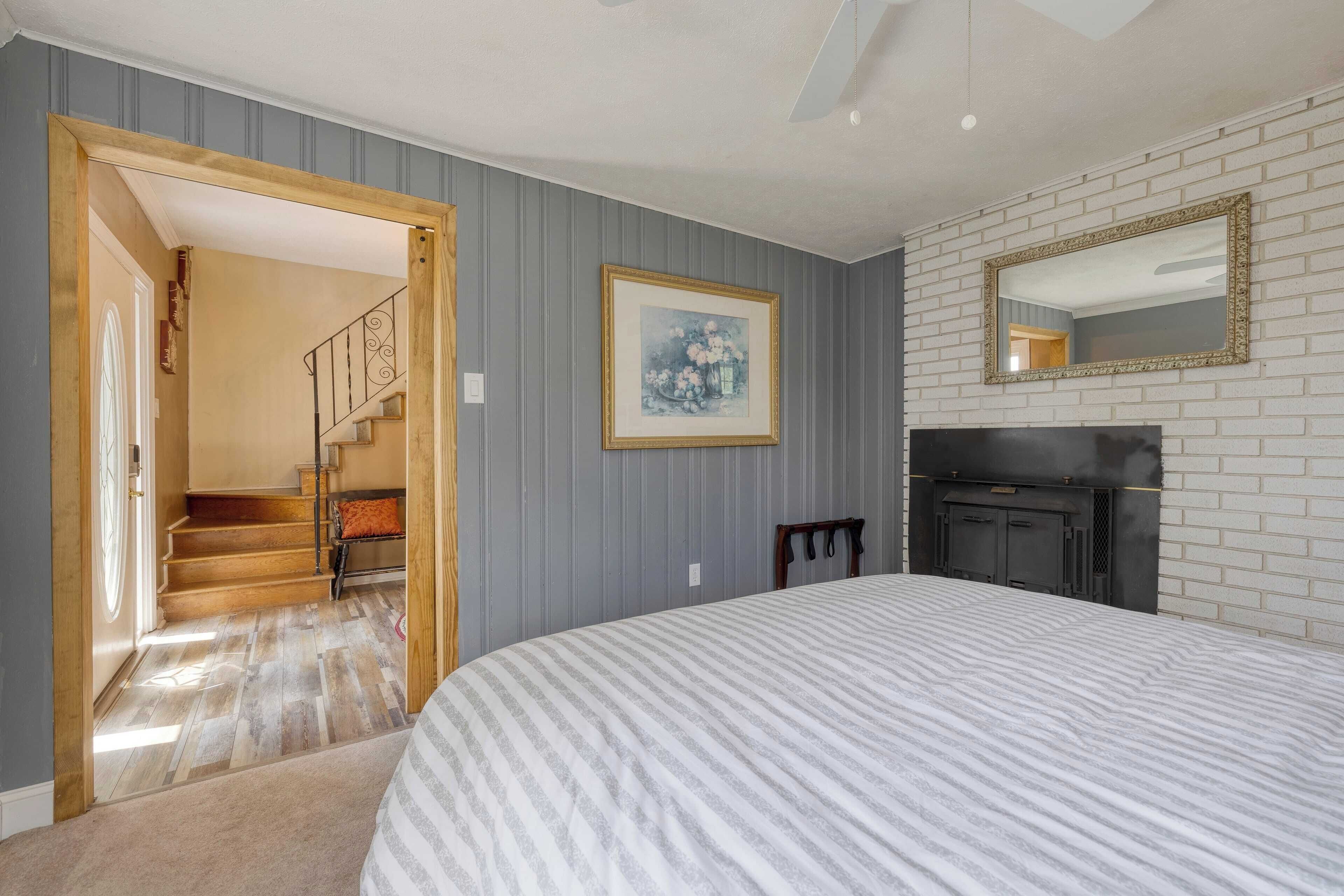 Une chambre à coucher avec un grand lit, une cheminée, un tableau encadré au mur et un escalier menant à une autre pièce.
