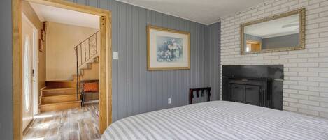 Une chambre à coucher avec un grand lit, une cheminée, un tableau encadré au mur et un escalier menant à une autre pièce.