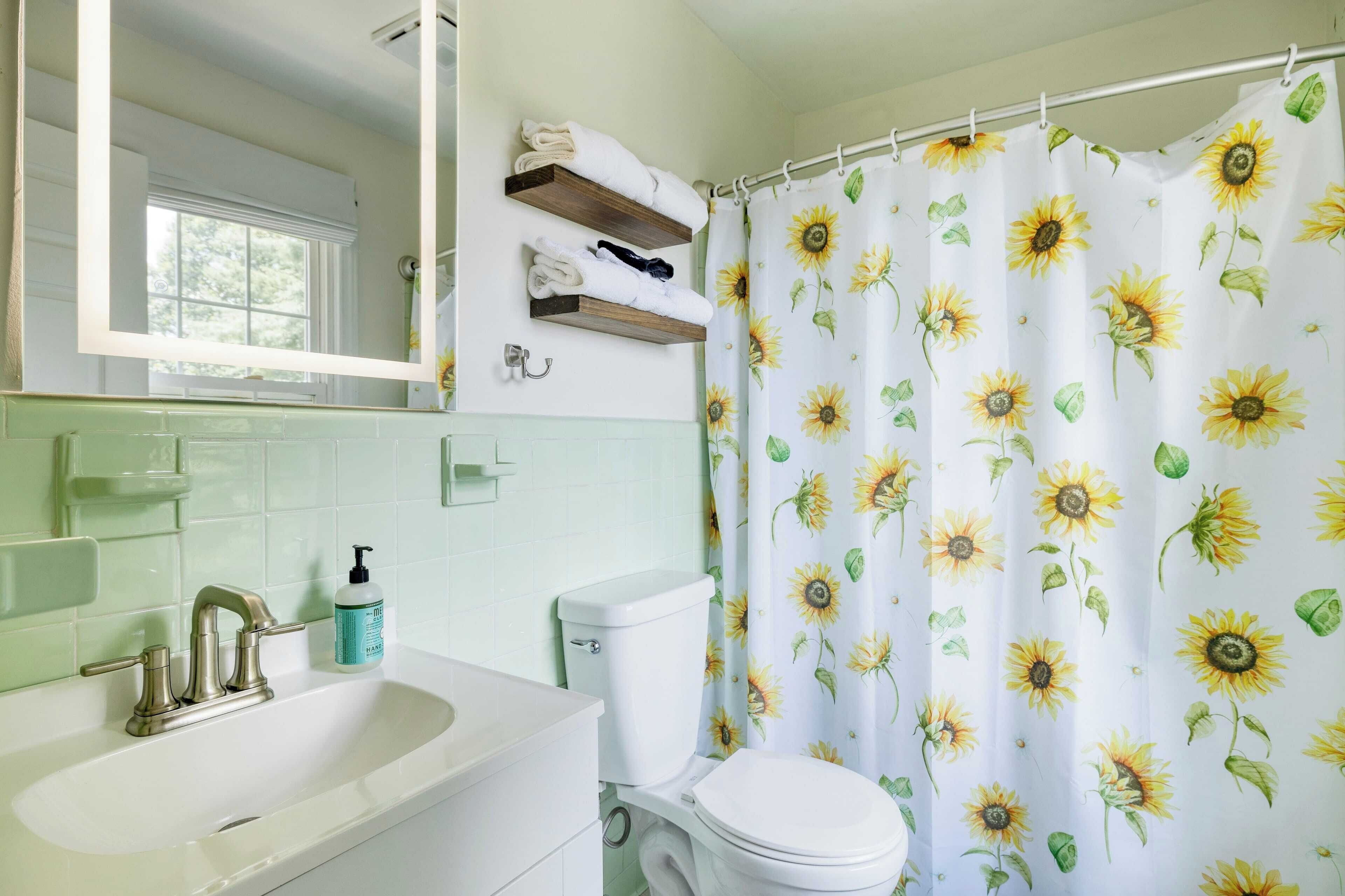 A bathroom with a sink, mirror, toilet, and shower curtain with a sunflower pattern.