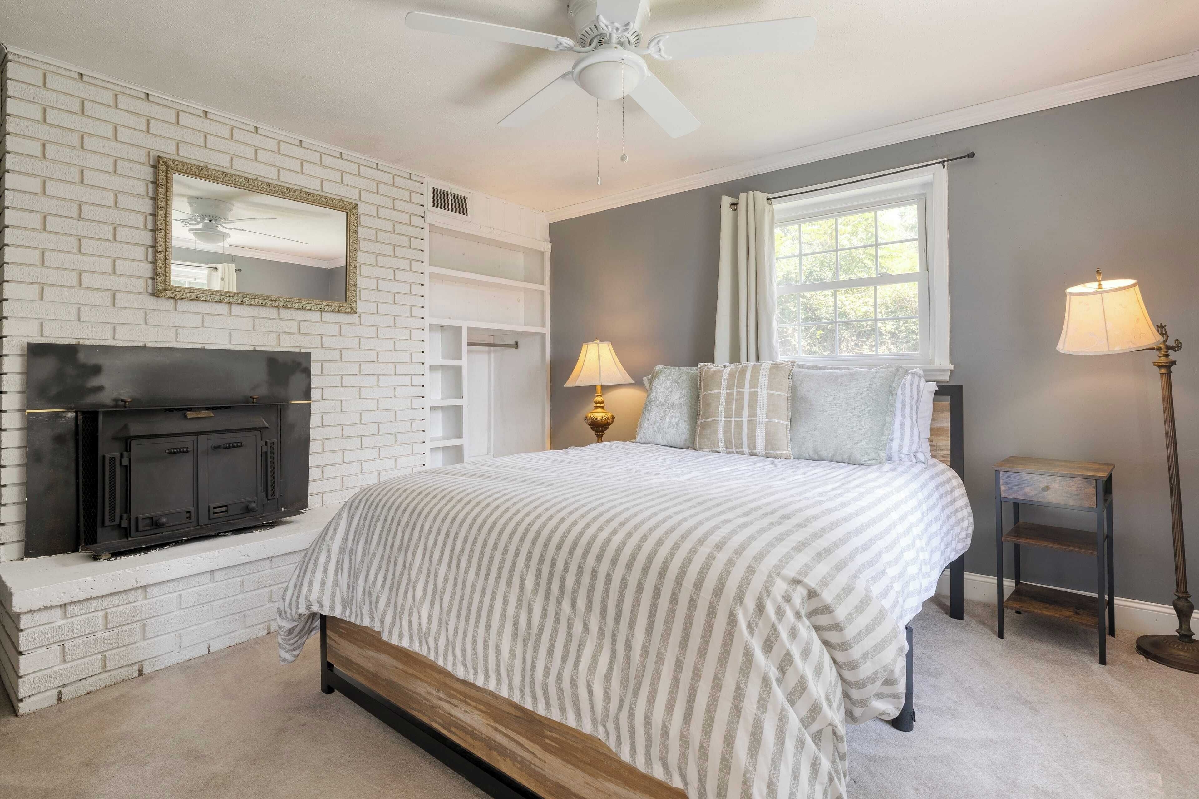 A bedroom with a fireplace, a bed with striped bedding, a ceiling fan, and two bedside lamps.