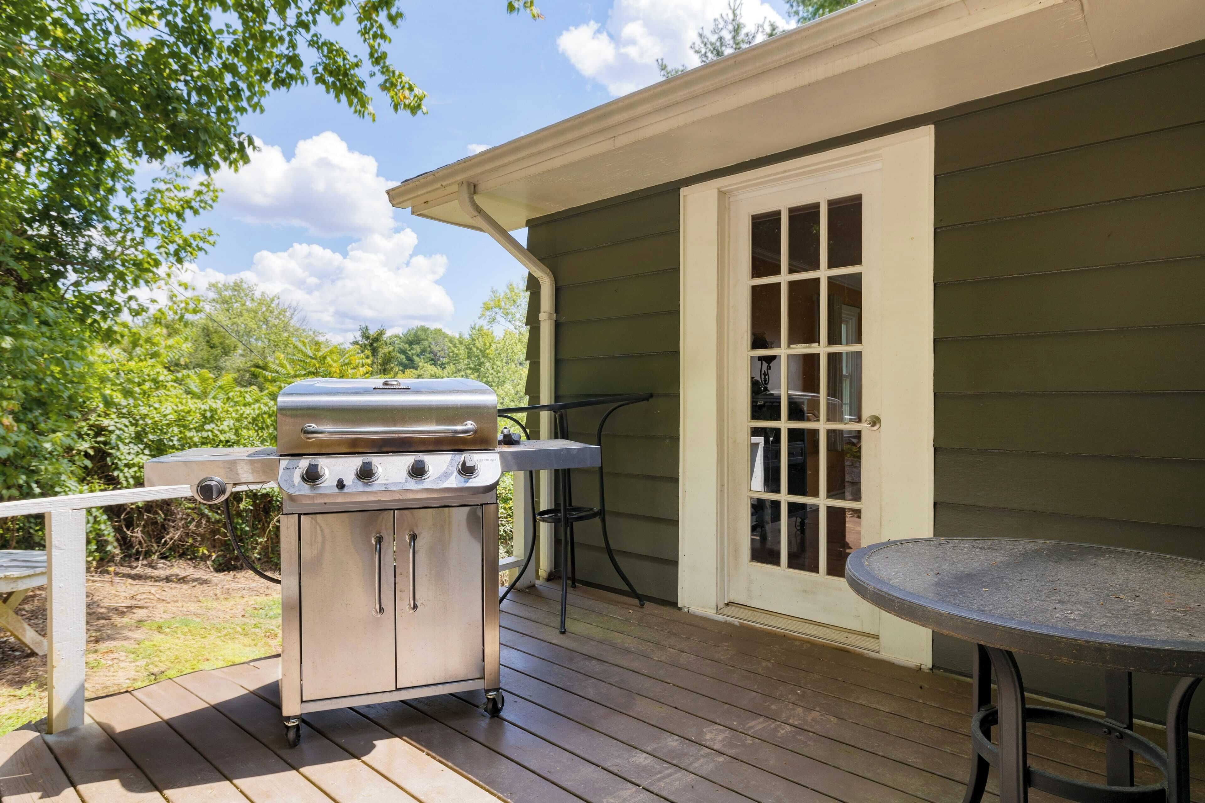 Un espacio al aire libre techado con una parrilla, una mesa y una puerta que da a una habitación.