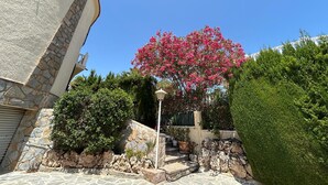 A stone building with a curved facade, a pink flowering tree, and a well-maintained garden with various plants and a stone staircase. - VILLA LOS ALMENDROS WITH PRIVATE POOL  (Calpe , Alicante)