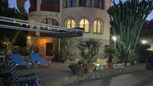 A building with a curved facade, multiple arched windows, and a stone wall. There are potted plants and a cactus in the foreground. - VILLA LOS ALMENDROS WITH PRIVATE POOL  (Calpe , Alicante)