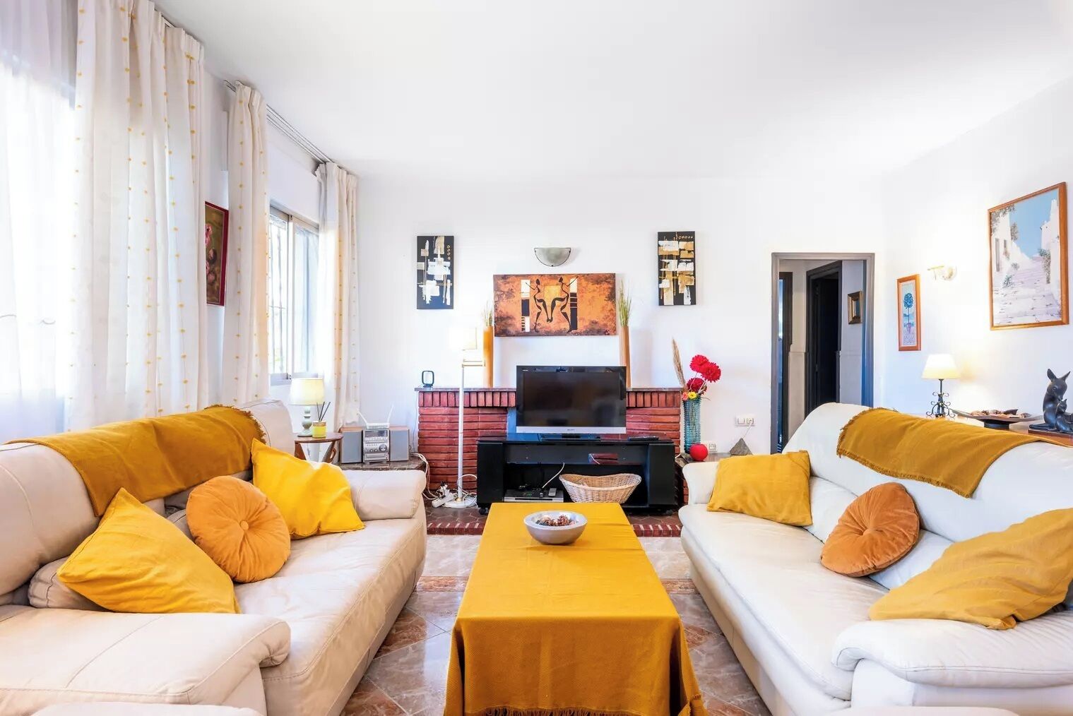 Ein Wohnzimmer mit zwei weißen Sofas, einem Couchtisch, einem Fernseher und einem Kamin.