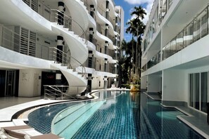 A modern hotel with a central swimming pool, multiple balconies, and palm trees. - B14 - 2 Bedroom Condo With Pool Access, Karon Beach (Karon)
