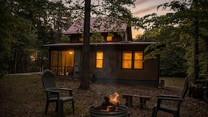 Uma cabana com lareira, área de estar externa e vista para a floresta ao redor.