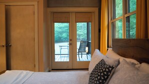 Quarto com cama, porta e vista para um deck externo com uma cadeira.