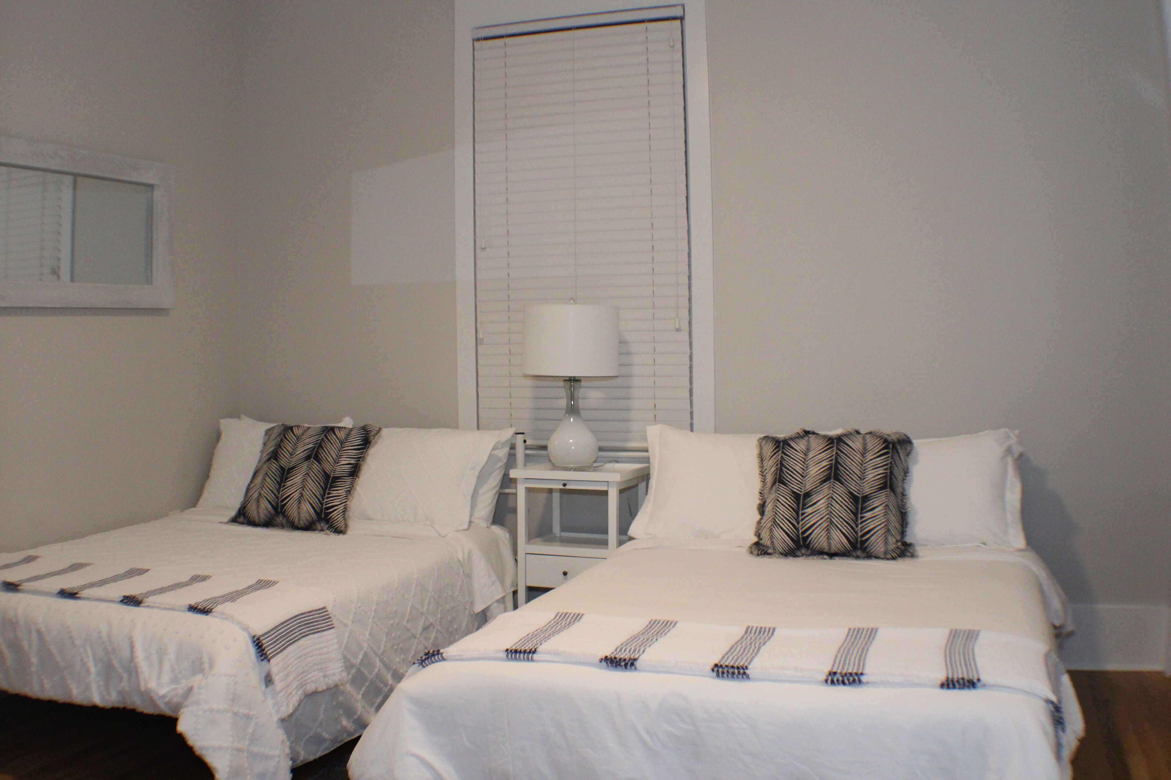 A hotel room with two single beds, a nightstand with a lamp, and a window with blinds.
