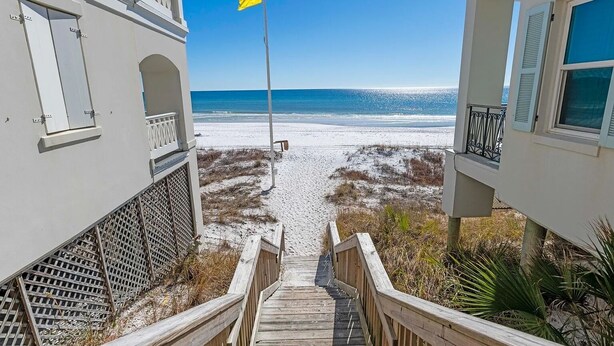 A wooden staircase leading to a beach with a flag in the distance. - Beautiful 4-br 3 king beds, 20 seconds to beach, community pool (Destin)