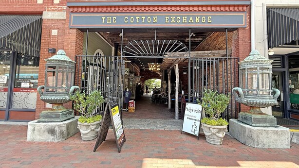 The entrance to The Cotton Exchange with a brick facade, wrought iron gates, and potted plants.