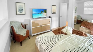 A bedroom with a bed, a television on a dresser, a chair, and a door leading to another room.