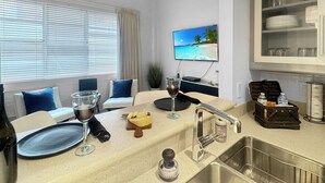 A modern kitchen with a sink, countertop, and a television displaying a beach scene.