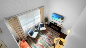 A modern living room with a fireplace, a flat-screen TV, and a colorful rug.