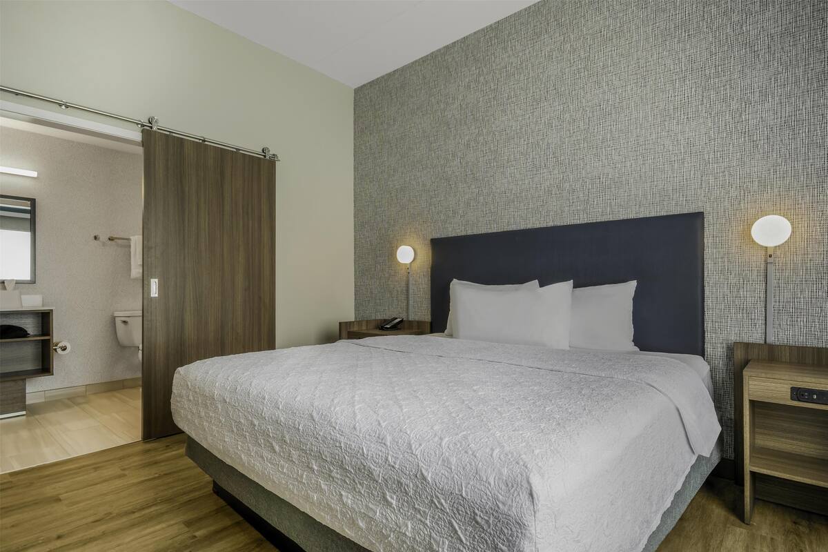 Een moderne slaapkamer met een groot bed, een houten hoofdbord en twee nachtkastjes met lampen.