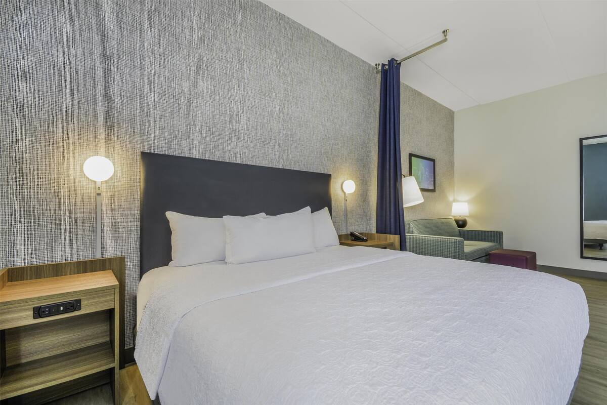 Een hotelkamer met een groot bed, twee nachtkastjes, een lamp en een televisie die aan de muur hangt.