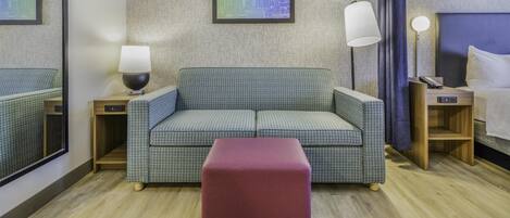 Ein Hotelzimmer mit einer gemusterten Couch, einem roten Hocker, einem Spiegel und einem Stadtbild an der Wand.