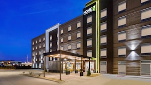 A modern hotel with a prominent "HOME 2" sign, covered outdoor seating area, and a well-lit entrance.