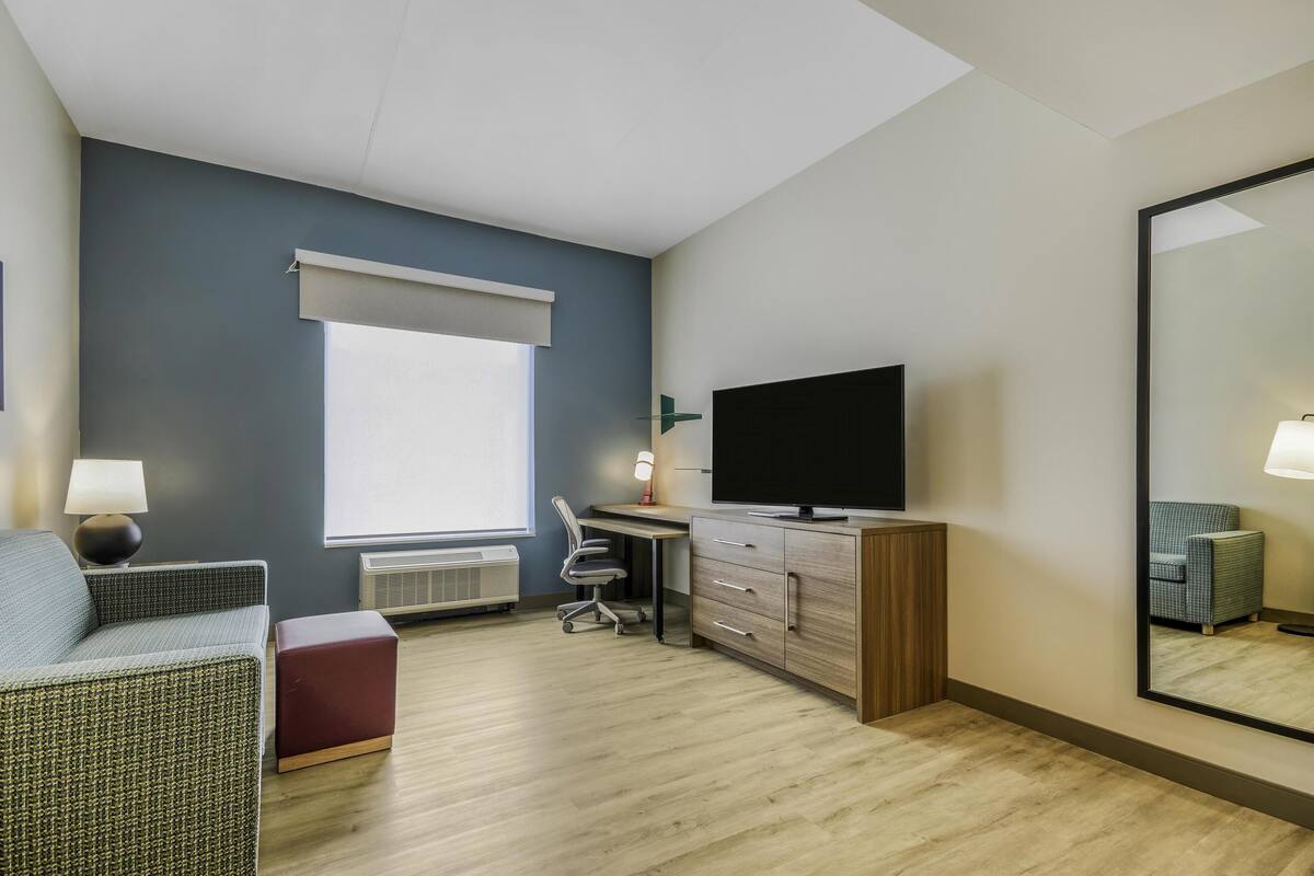 Een moderne hotelkamer met een groot bed, een bureau met een computer, een televisie, een stoel en een grote spiegel.