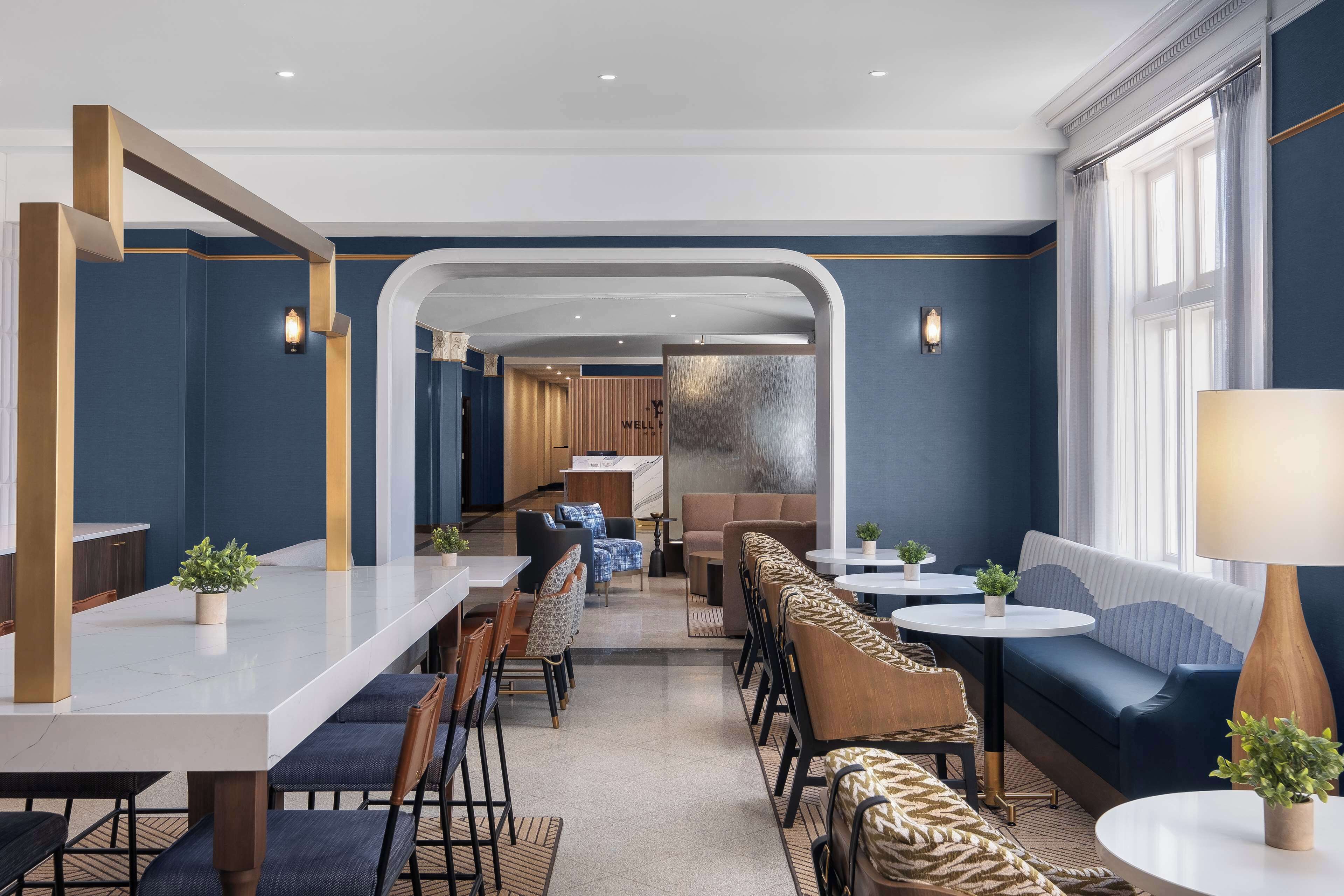 Un moderno hall de hotel con un mostrador de recepción alargado, zonas de estar y vista al interior.