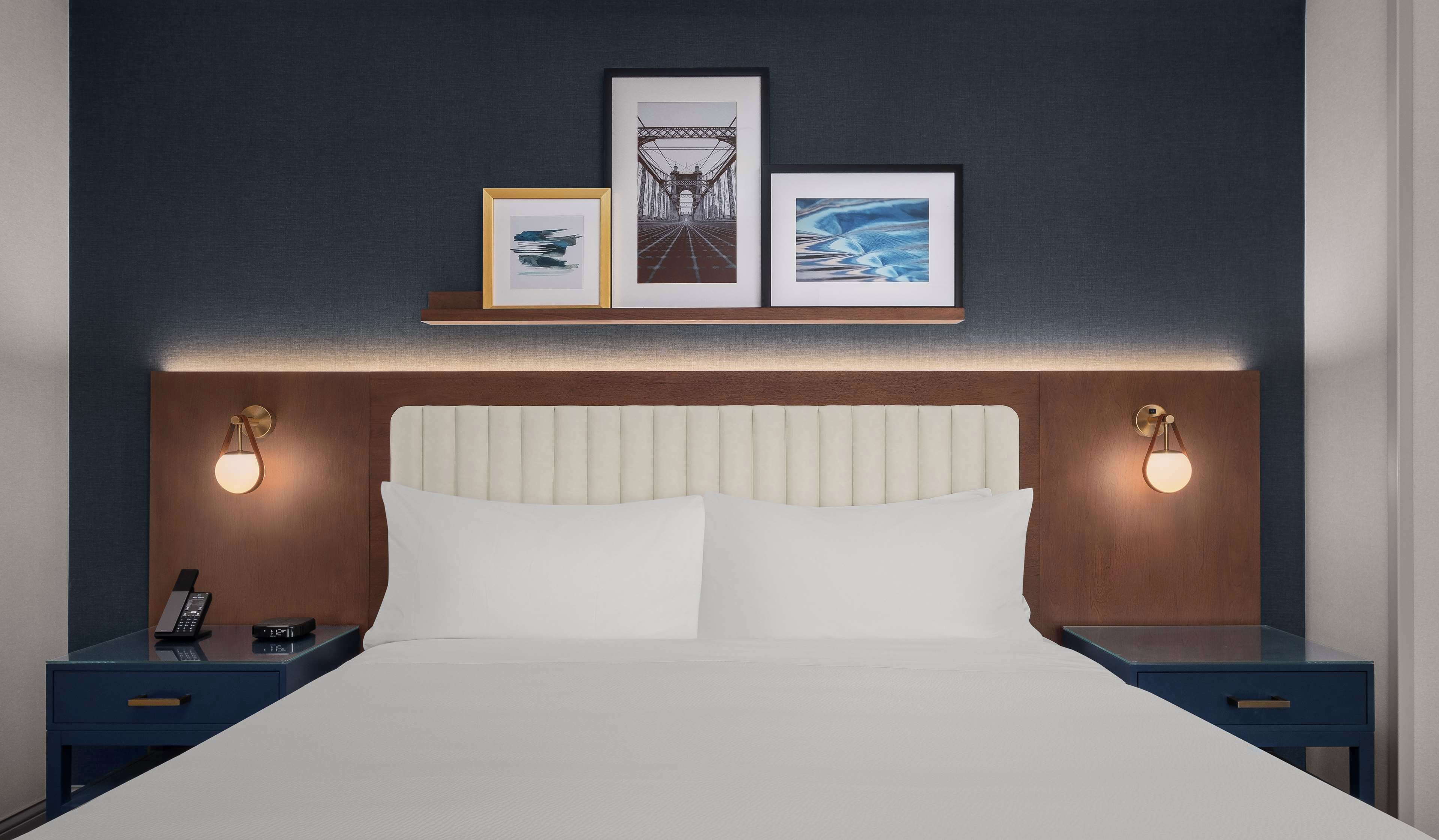 A hotel room with a large bed, two bedside tables with lamps, a phone, and framed artwork on the wall.