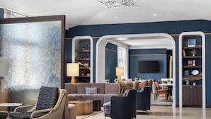 Un hall d’hôtel moderne avec un canapé, des fauteuils, une table basse et un téléviseur fixé au mur.