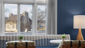 Une pièce avec une grande fenêtre, un mur bleu, une table en bois et un banc agrémenté d’une plante.
