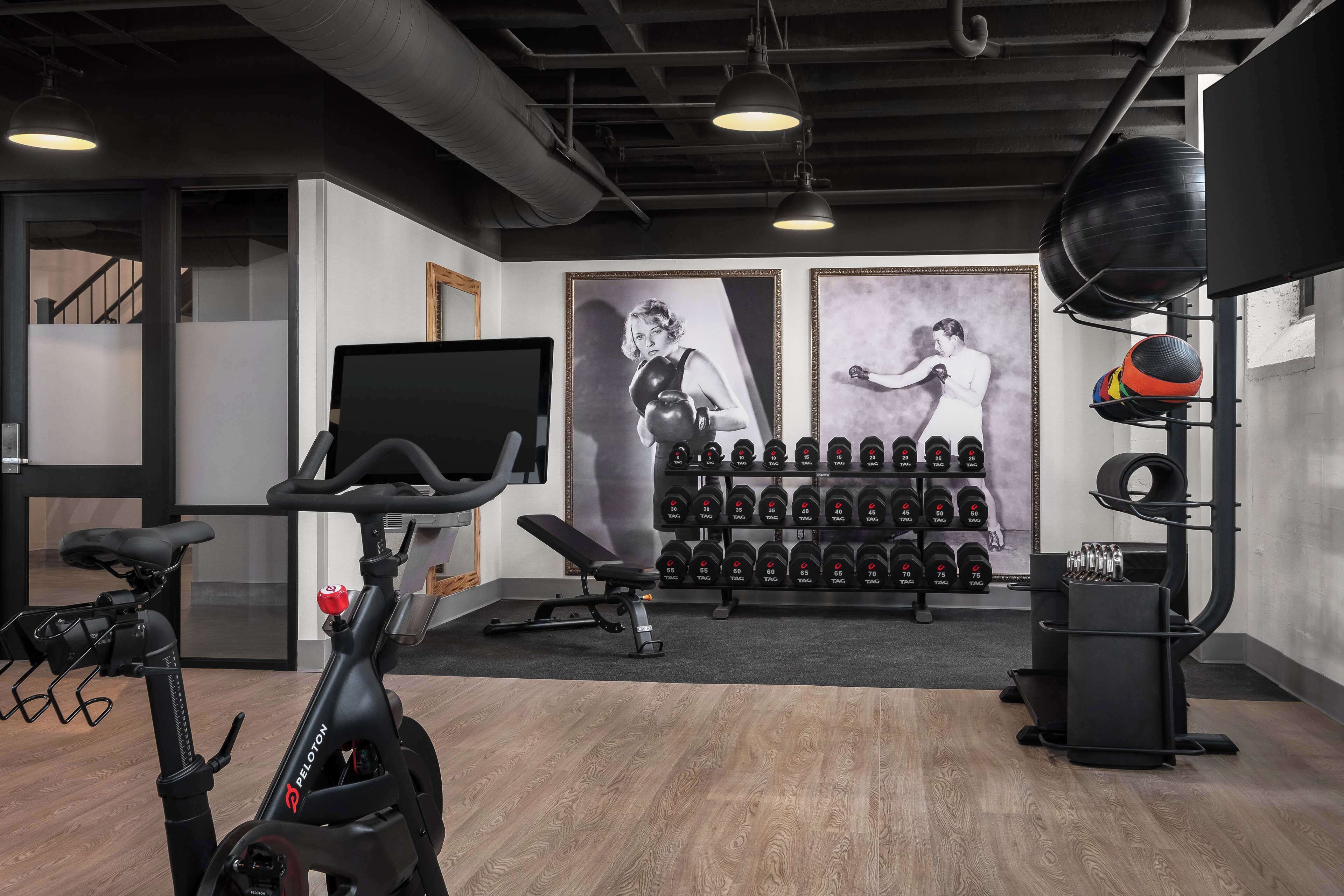 A gym with exercise equipment, a wall-mounted TV, and a rack of dumbbells.