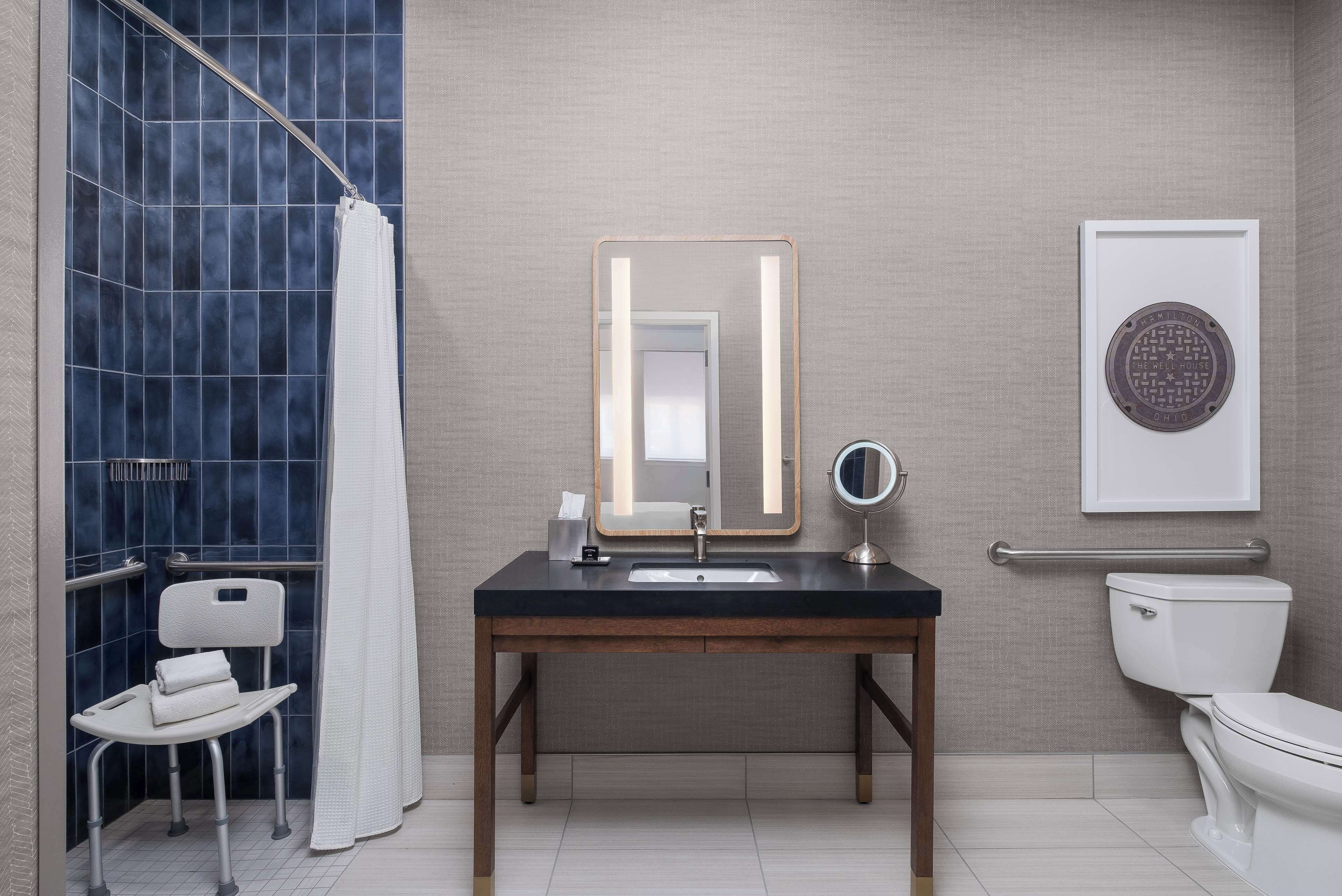 Un baño con ducha, lavabo con espejo, inodoro y una silla accesible para sillas de ruedas.
