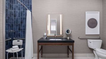 Un baño con ducha, lavabo con espejo, inodoro y una silla accesible para sillas de ruedas.