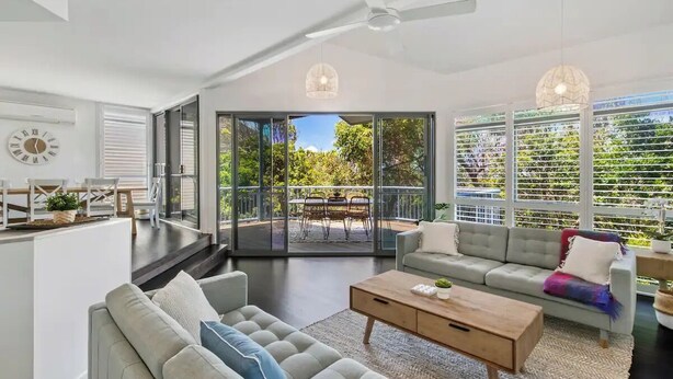 A spacious living area with a sofa, coffee table, and a balcony with a dining set. - Seaside Home- Direct beach access & pet friendly (Noosa)