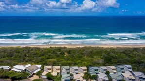 A coastal view with a beach and ocean. There are multiple buildings with flat roofs, likely part of a resort or hotel. - Seaside Home- Direct beach access & pet friendly (Noosa)