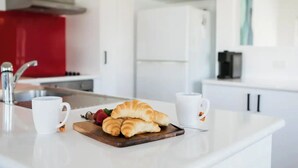 Eine moderne Küche mit weißen Schränken, einer roten Akzentwand und einem Schneidebrett mit Croissants und Erdbeeren.