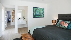 Ein Schlafzimmer mit Bett, Nachttisch, einem an der Wand hängenden Bild und einem durchgehenden Türspalt sichtbaren Badezimmer.