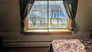 Une chambre avec une grande fenêtre, un lit recouvert d’une couvre-lit à motifs et un radiateur placé sous la fenêtre.