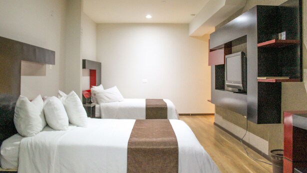 A hotel room with two beds, a TV mounted on the wall, and a small shelf with items. - Hotel Cancalli Tlaxcala (Tlaxcala)