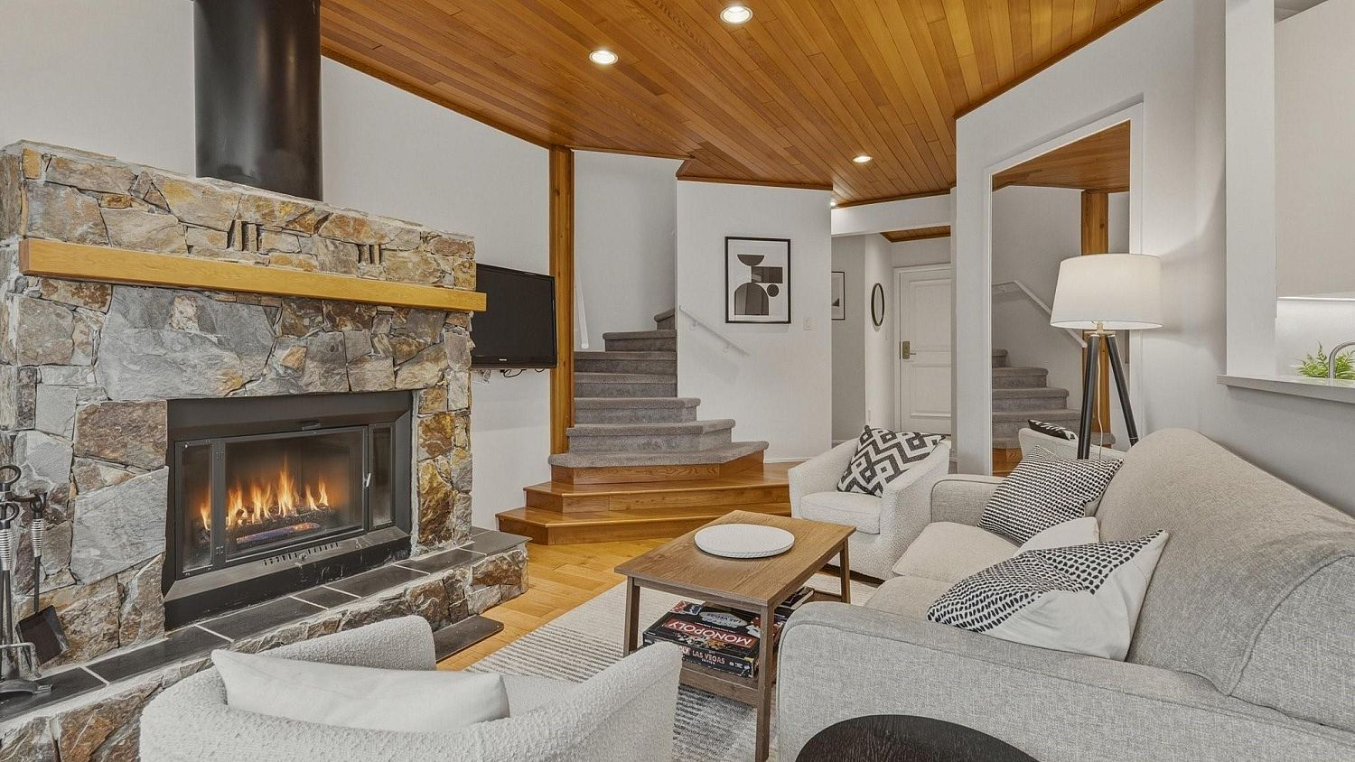 A living room with a stone fireplace, a staircase, and a sofa.